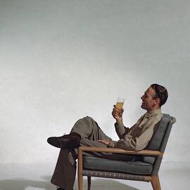 A Man Sitting In An Armchair With A Drink by John Rawlings