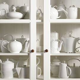 Assorted Tea And Coffee Pots In A Glass Cupboard by Sivan Lewin