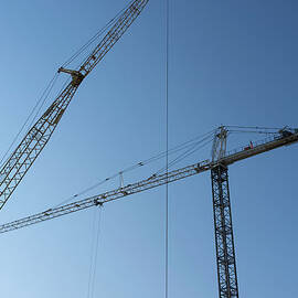 Construction Cranes Against A Blue Sky by Alvis Upitis