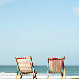 Deck Chairs On Coastline Facing Out To by Dougal Waters