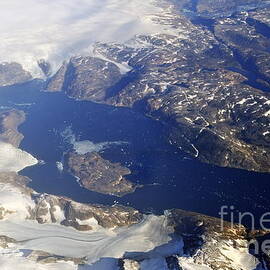 Snowy rocky coastline and floating icebergs on ocean by Sami Sarkis Photography