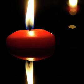 Burning candle reflected by water at night by Sami Sarkis Photography