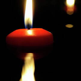 Burning candle reflected by water at night by Sami Sarkis Photography
