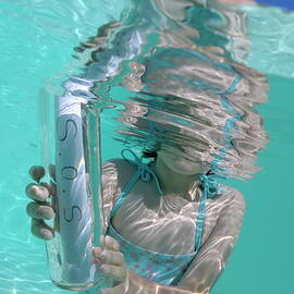Girl in pool holding bottle with SOS message by Sami Sarkis Photography