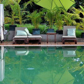 Wooden seats and umbrella reflected in pool by Sami Sarkis Photography