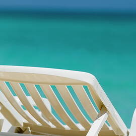 Empty white deck chair on a beach by Sami Sarkis Photography
