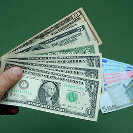Close-up of man's hand with US banknotes and Euro banknotes by Sami Sarkis Photography