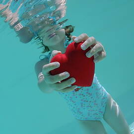 Girl holding heart shaped symbol in swimming pool by Sami Sarkis Photography