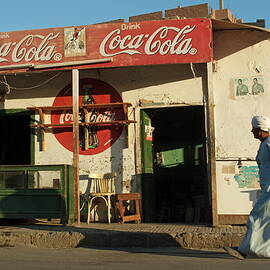 Man dressed in traditional Islamic dress walks by a coffee shop in Egypt by Sami Sarkis Photography