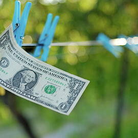 Man's hand taking one US dollars banknote hanging on clothesline by Sami Sarkis Photography