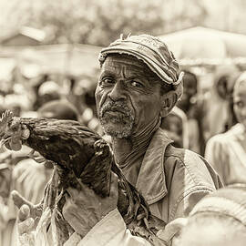 Old ethiopian man selling a rooster in a market by Miroslav Liska