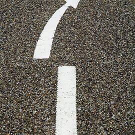 Painted white arrow sign in the dividing line on the road by Sami Sarkis Photography