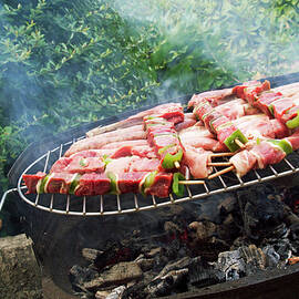 Sausages and meat on skewers grilling on a barbeque outside by Sami Sarkis Photography
