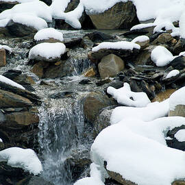 Snow-covered rocks beside a mountain stream in the French Alps by Sami Sarkis Photography
