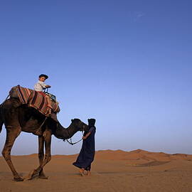Touareg man leading boy riding camel in Sahara Desert by Sami Sarkis Photography