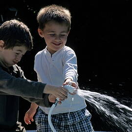 Two boys playing with garden hose by Sami Sarkis Photography