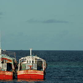 Two red fishing boats moored side by side in the blue ocean by Sami Sarkis Photography