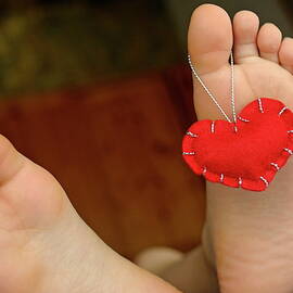 Valentine heart hanging on girl's barefeet by Sami Sarkis Photography
