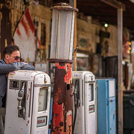Young man smokes a cigarette at a vintage gas pump by Miroslav Liska