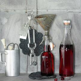 An Arrangement Of Cherry-vanilla Syrup In Bottles And Kitchen Utensils by Jalag / Wolfgang Kowall