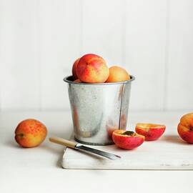 Apricots In A Metal Container And Next To It, One Halved by Magdalena Hendey
