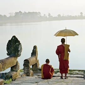 Buddhist Monks Standing On Waters Edge by Martin Puddy