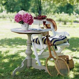 Cherries And Hydrangeas On Round Wooden Table And Tennis Racquets Leaning On Chair In Sunny Garden by Tine Guth Linse