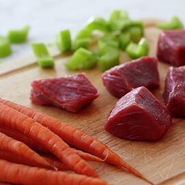 Chunks Of Raw Beef, Raw Carrots And Chopped Celery On A Wooden Cutting Board by Edward Thomas