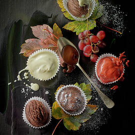 Ice Cream Desserts And Vanilla Sauce In Paper Cases, Grapes And Autumnal Leaves On A Black Surface by Manfred Rave