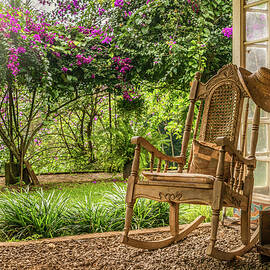 A vintage wooden rocking chair with a straw hat rests on a porch by Steven Heap