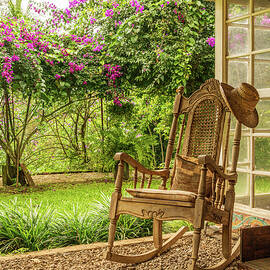 A vintage wooden rocking chair with a straw hat rests on a porch by Steven Heap