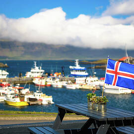 Flag of Iceland placed on a restaurant table with a harbor in the background by Miroslav Liska