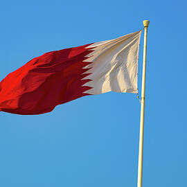 Qatar national flag waving on flagpole against clear blue sky by Miroslav Liska