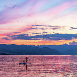 Sunset over Lake Chelan with silhouette of couple paddling on pa by Steven Heap