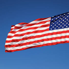 USA flag waving in the wind against a cloudless blue sky by Miroslav Liska
