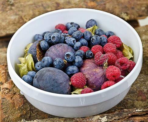 A Fruit Bowl With Figs, Blueberries And Raspberries On A Wooden Surface Print