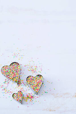A Set Of Three Heart Cookie Cutters Filled With Colorful Sprinkled On A White Surface Print