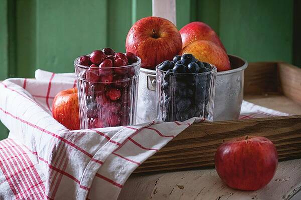 An Aluminium Bowl Of Red Apples And Glasses Of Blackberries And Lingonberries On An Old White Wooden Chair Against The Green Wooden Walled Print