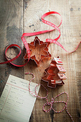 Copper Christmas Shaped Cookie Cutters On A Rustic Wooden Surface With Red Noel Ribbon Bakers Twine And Cookie Recipe Print