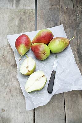 Several Pears, Whole And Halved, On Grease-proof Paper With A Knife Print