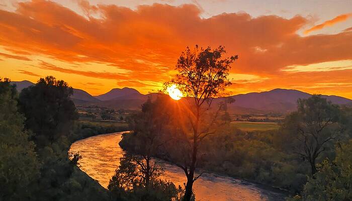 Mountain Wall Art featuring the digital art River Valley With Trees Under A Red And Orange Sunset Sky - Digital Painting by Nicko Prints