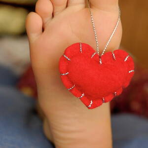 Valentine heart hanging on girl's barefeet #1 by Sami Sarkis Photography